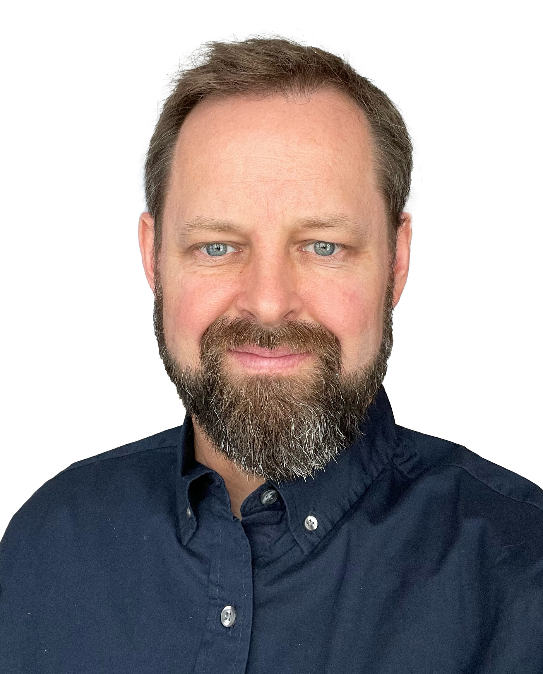 Lee Keenan wearing a dark blue button up shirt. He is smiling, standing in front of a white background. Lee Keenan wearing a dark blue button up shirt. He is smiling, standing in front of a white background.
