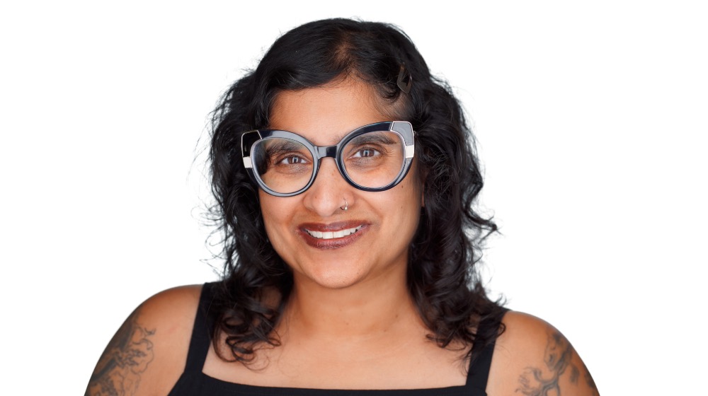 Dr. Sarita smiles standing in front of a white background. Dr. Sarita smiles standing in front of a white background.