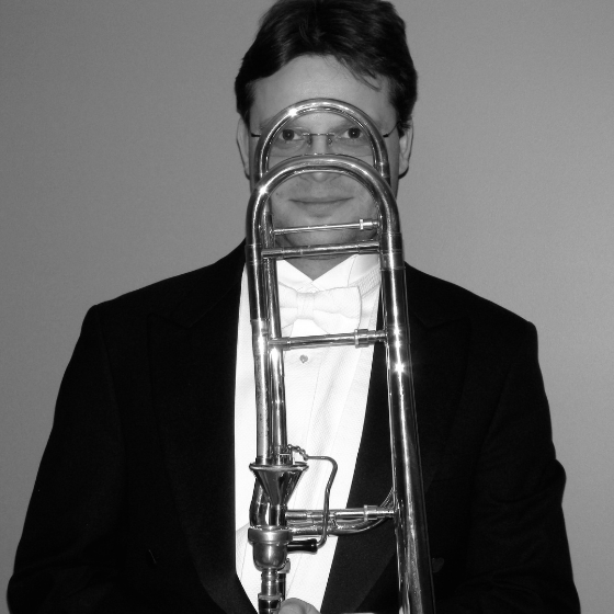 Monochrome image of a man in a suit, smiling and holding a trombone in front of his face. Monochrome image of a man in a suit, smiling and holding a trombone in front of his face.