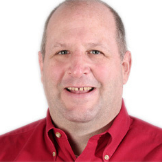 A smiling man wearing a red collared top, against a solid white background. A smiling man wearing a red collared top, against a solid white background.