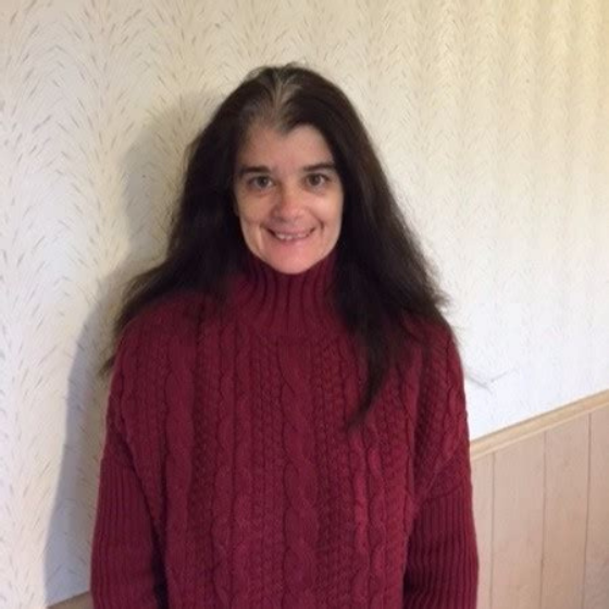Smiling woman with brown hair, wearing a dark red sweater, standing in front of an off-white background. Smiling woman with brown hair, wearing a dark red sweater, standing in front of an off-white background.