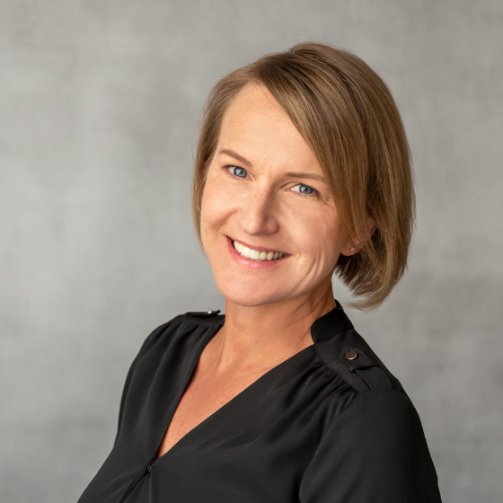 Smiling woman with short dark blonde hair, wearing a black top, against a grey background. Smiling woman with short dark blonde hair, wearing a black top, against a grey background.