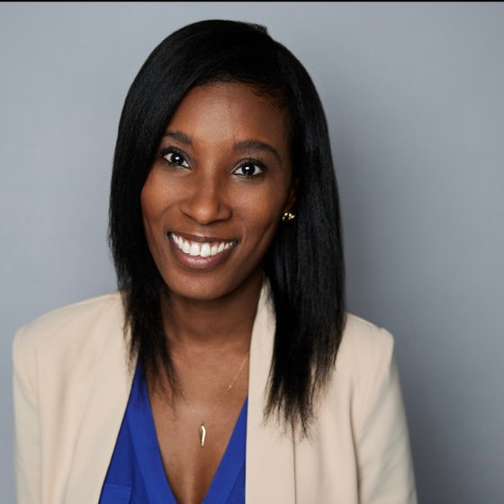 Smiling woman with shoulder length straight black hair, wearing an off-white blazer over a purple top, against a solid grey background. Smiling woman with shoulder length straight black hair, wearing an off-white blazer over a purple top, against a solid grey background.