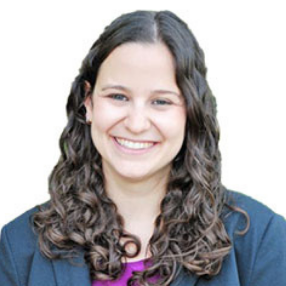 A smiling woman with medium length, wavy brown hair, wearing a dark blue blazer over a magenta top, behind a solid white background. A smiling woman with medium length, wavy brown hair, wearing a dark blue blazer over a magenta top, behind a solid white background.