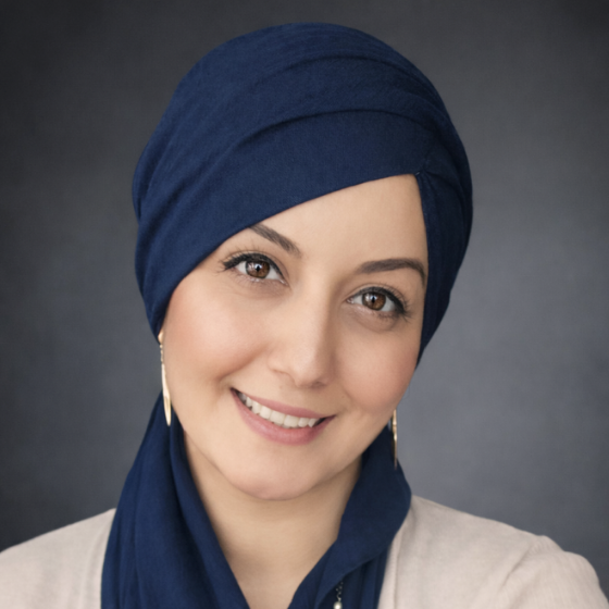 Smiling woman with a navy blue headscarf, wearing a white top, against a dark grey background. Smiling woman with a navy blue headscarf, wearing a white top, against a dark grey background.