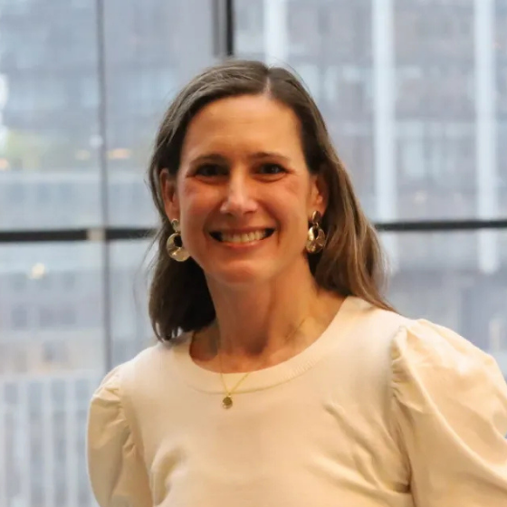 A woman smiling with shoulder-length dark blonde hair, wearing an off-white blouse, with a window in the background. A woman smiling with shoulder-length dark blonde hair, wearing an off-white blouse, with a window in the background.