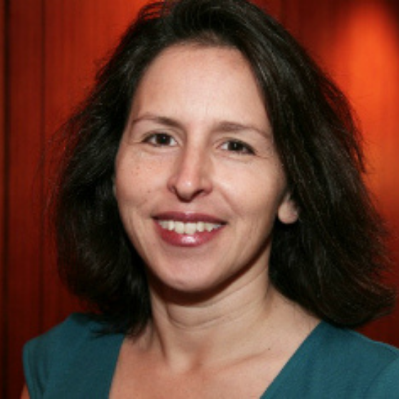 A woman smiling with shoulder-length brown hair, wearing a teal top, against a dark red wall. A woman smiling with shoulder-length brown hair, wearing a teal top, against a dark red wall.