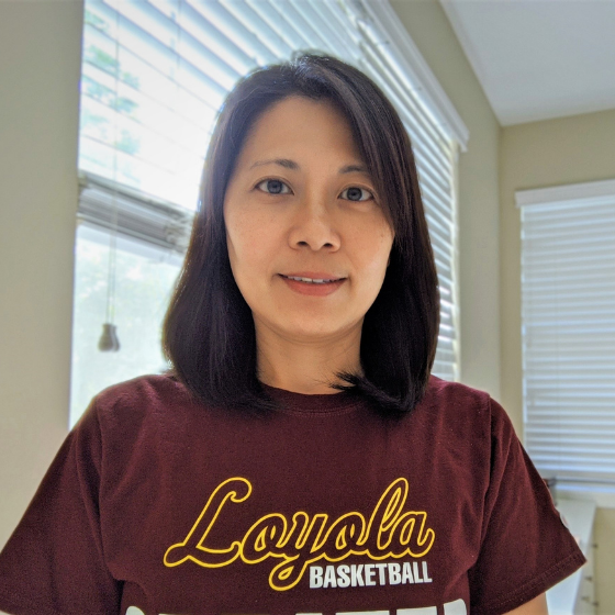 A woman with shoulder-length brown hair, smiling slightly, wearing a maroon Loyola University Chicago top, with a bright sunroom in the background. A woman with shoulder-length brown hair, smiling slightly, wearing a maroon Loyola University Chicago top, with a bright sunroom in the background.