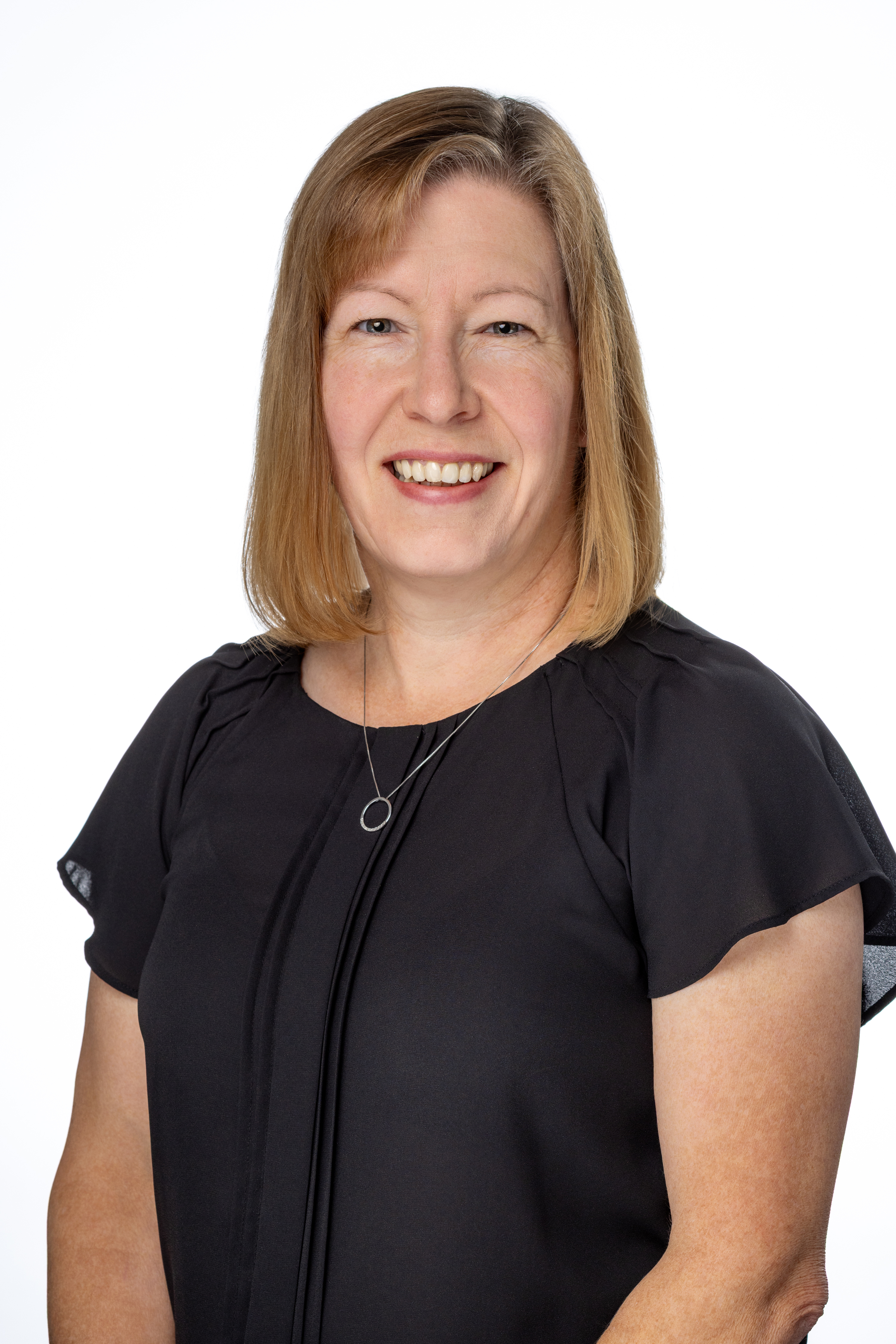 Christie Mason, a woman with shoulder-length light brown hair, wearing a black short-sleeve blouse and a simple circular pendant necklace, smiling against a light gray background. Christie Mason, a woman with shoulder-length light brown hair, wearing a black short-sleeve blouse and a simple circular pendant necklace, smiling against a light gray background.