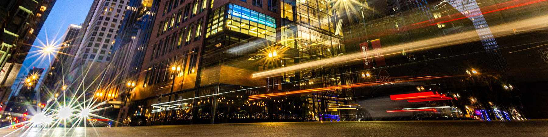 The evening sky reflects in the windows of Water Tower campus buildings at dusk while streaking red and gold vehicle lights and commuters pass in the foreground. The evening sky reflects in the windows of Water Tower campus buildings at dusk while streaking red and gold vehicle lights and commuters pass in the foreground.