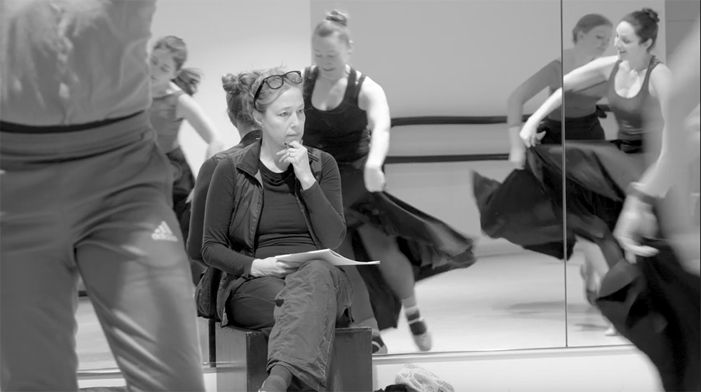 Sandra Kaufmann, sitting against the mirrored wall, watches dance students as they dance near her.