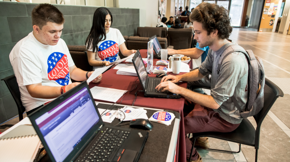 Two students help their peer register to vote.