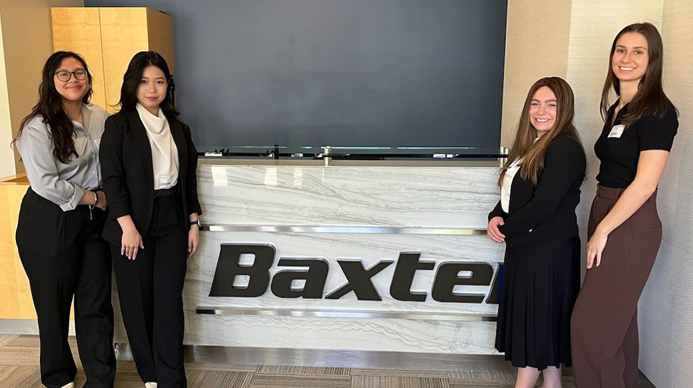 Class of 2024 students Lauren David, Dhruv Patel, Leah Smith, Esther Wayntraub, and Elza Wu pose together in front of a Baxter display.