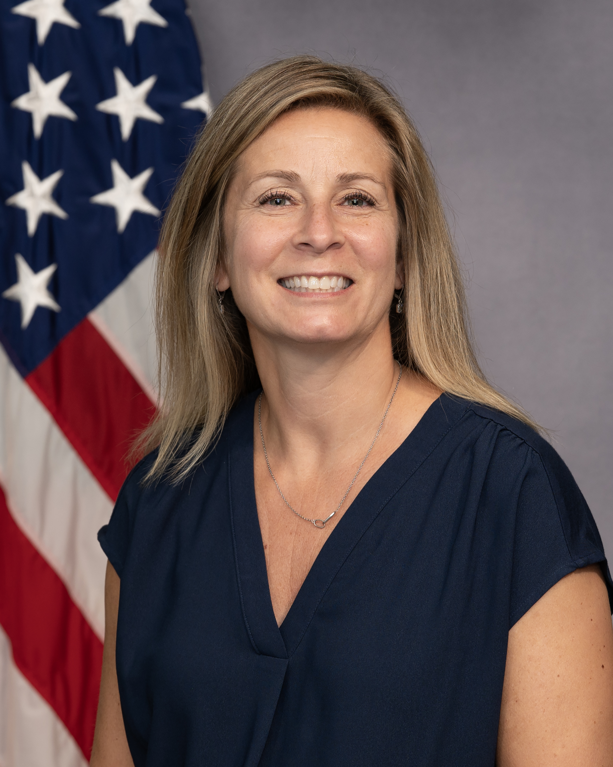 A blond person in a blue shirt in front of an American flag