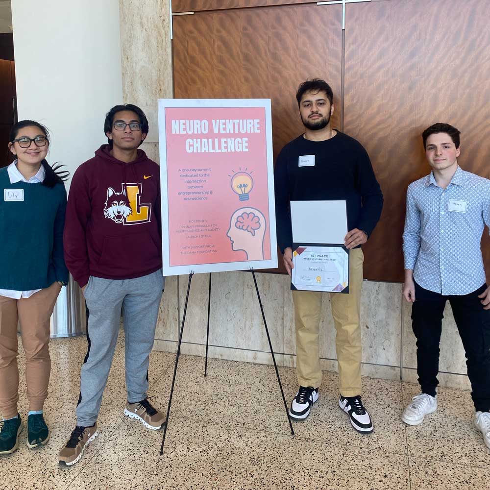 four student posing next to the NeuroVenture Challenge poster holding a first place prize