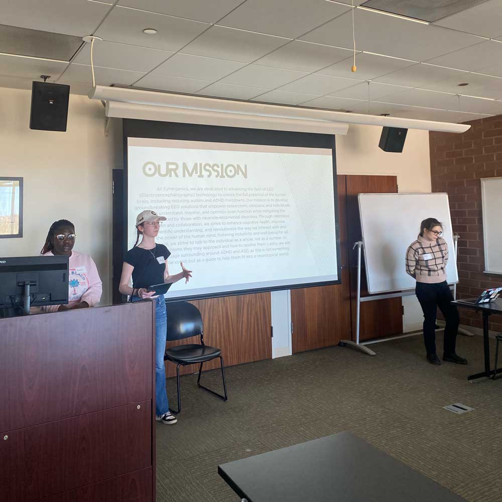 three female students presenting thier project, with a powerpoint slide titled 