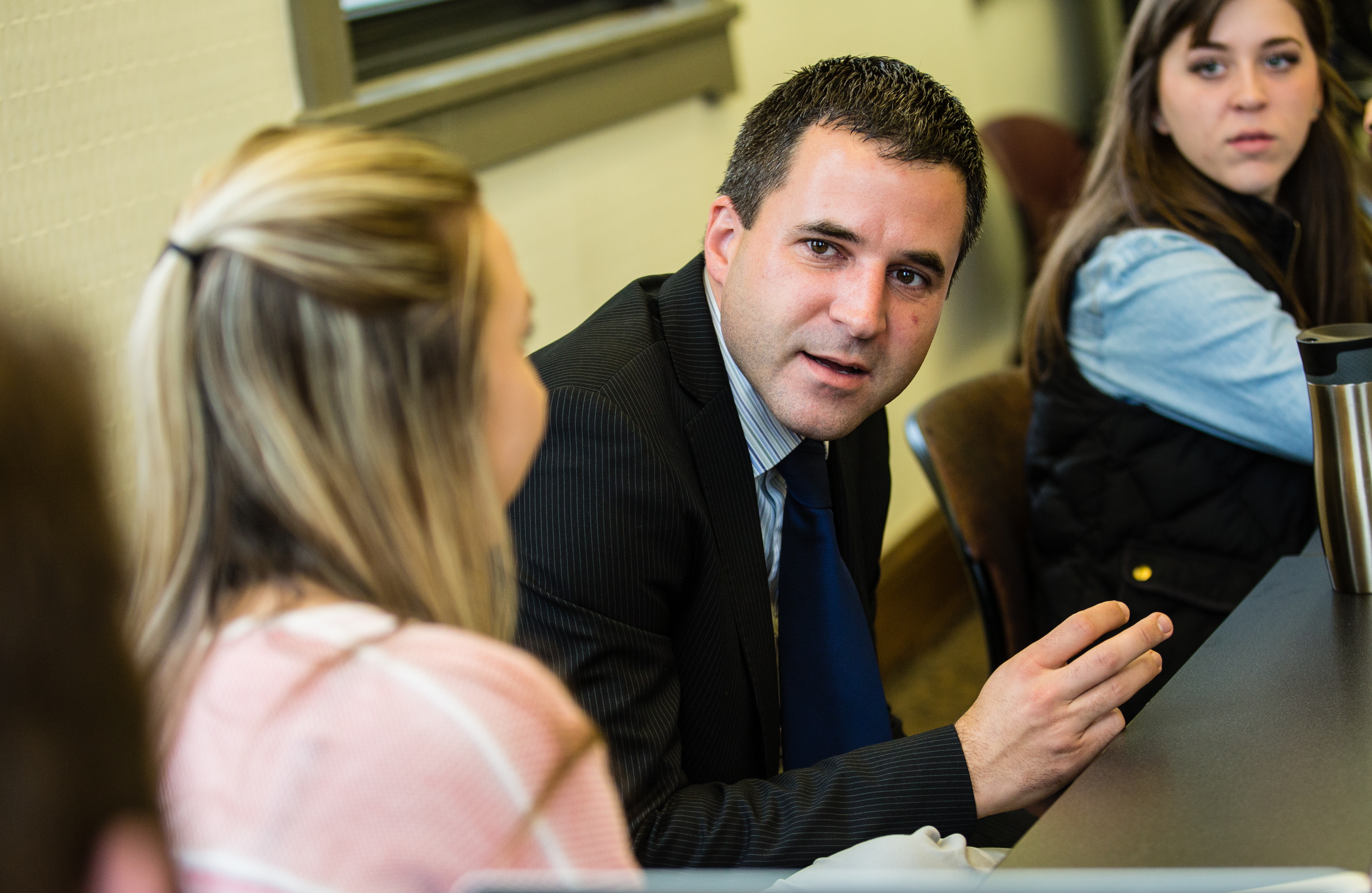 A student looks at another who has their back turned to the camera and they are mid conversation. Another student listens to them in the background.