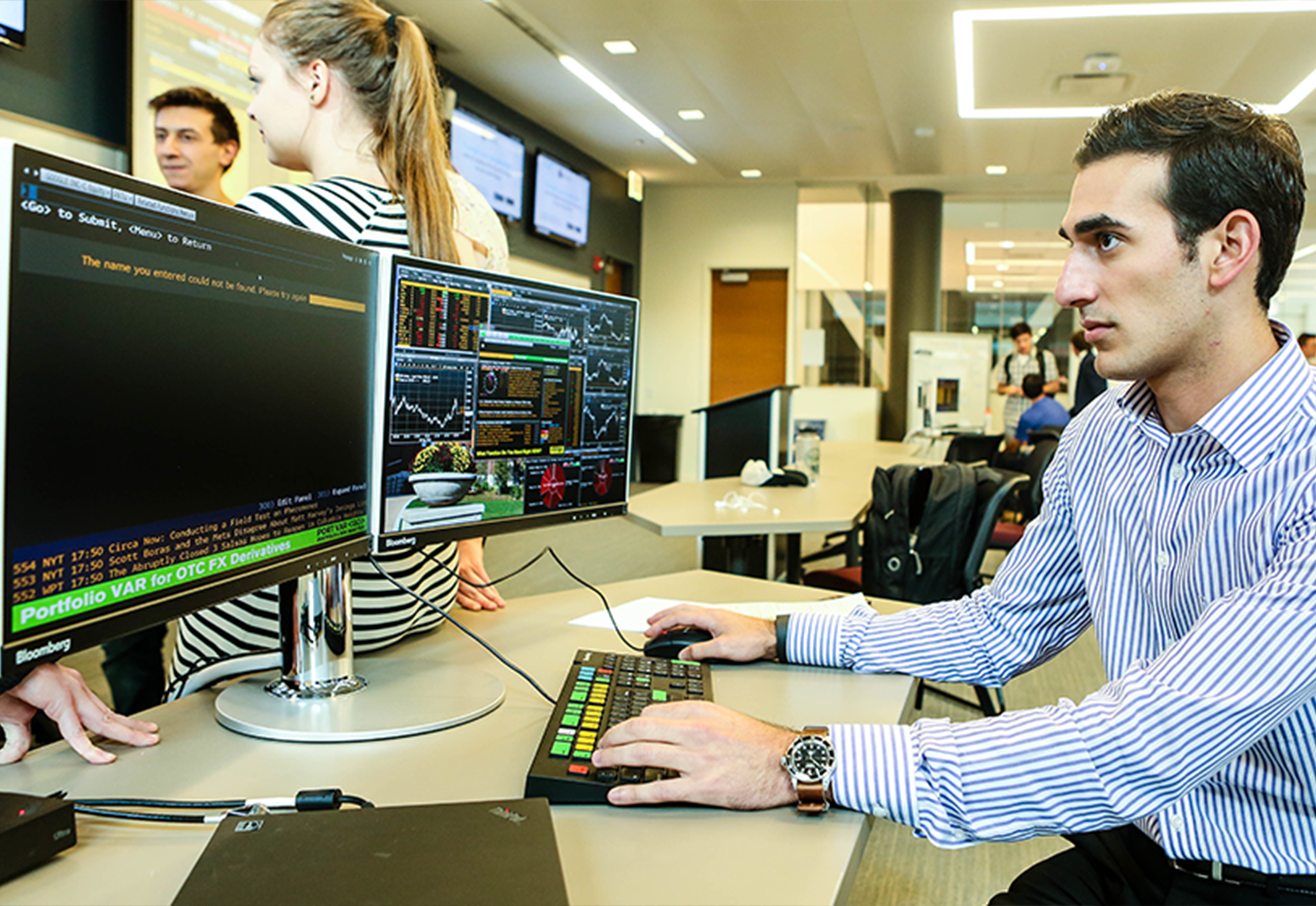 A man sits at a desk facing two monitors