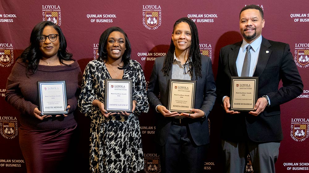 Four award winners smiling while holding their awards and standing in front of a Quinlan School of Business backdrop Four award winners smiling while holding their awards and standing in front of a Quinlan School of Business backdrop
