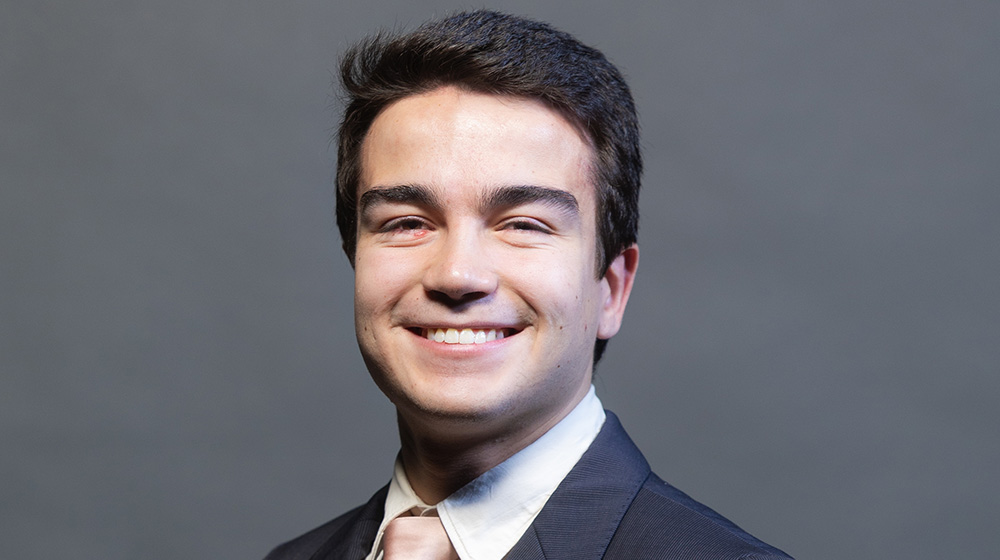 Headshot of João Barreto on a greay background. He's wearing a dark grey suit with a light pink tie.