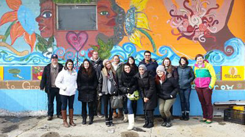 A group of students in casual winter attire gather for a group photo in front of a colorful mural on a wall