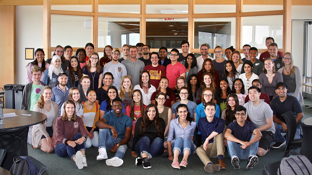 A large group of students poses for a photo in casual attire. Some are standing in the back while others are seated in the front.