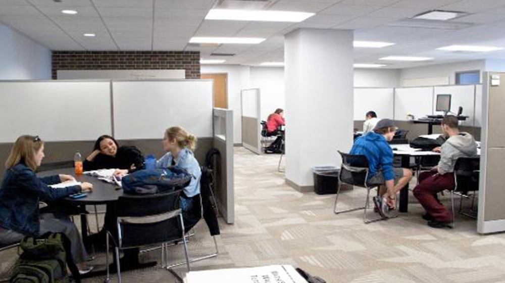 Students gather inside of an office space at tables in groups of three