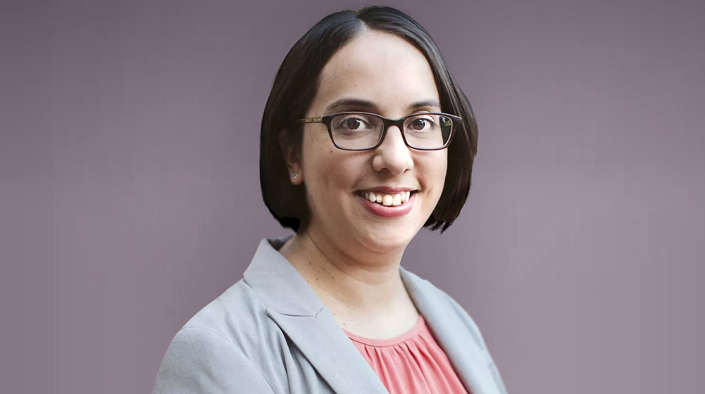 A portrait of Malini Suchak Dean School of Environmental Sustainability 2025. She is wearing black frame glasses, a gray coat and a coral blouse.