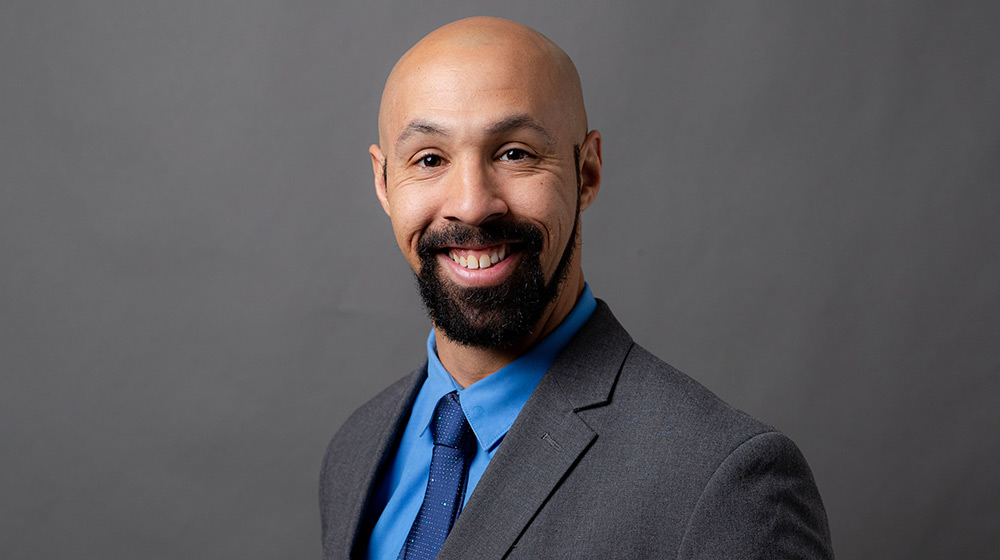 MVSS Director Alex Pirila smiling for a headshot photo in a grey suit with a blue tie and shirt.