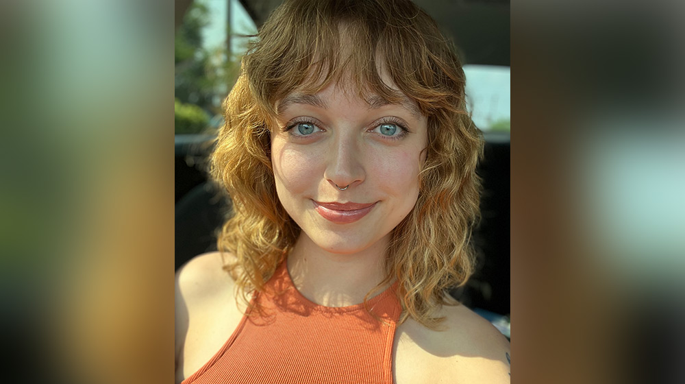 MVSS Assistant Director Lily Hasler smiling against an out-of-focus background in a orange shirt.