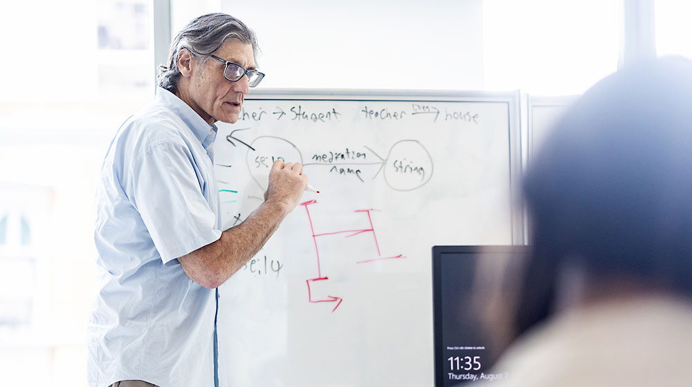 An instructor writes on a whiteboard teaching students in the classroom artificial intelligence and ethics. An instructor writes on a whiteboard teaching students in the classroom artificial intelligence and ethics.